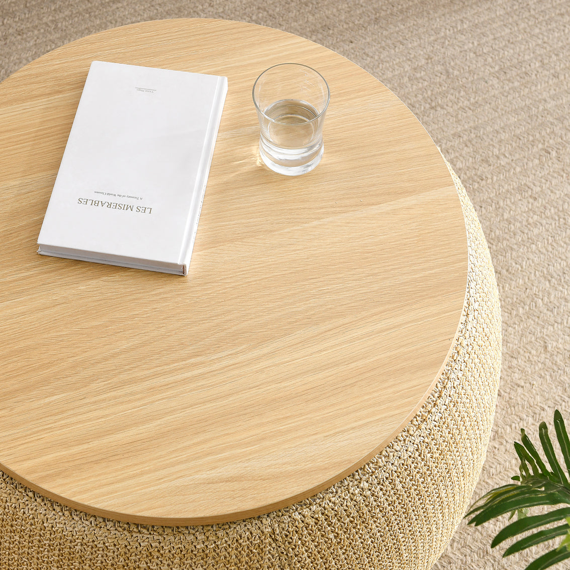 Round wooden side table with a glass of water and a book on a beige carpet.