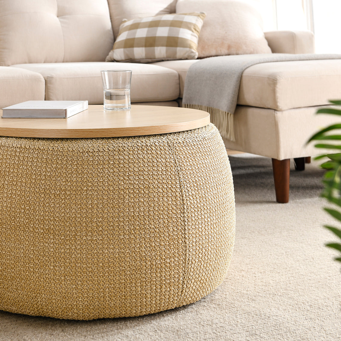 Beige textured ottoman with a glass of water on a wooden surface in a living room setting.