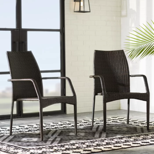 Two black wicker chairs on a patio with a glass door and plant in the background.