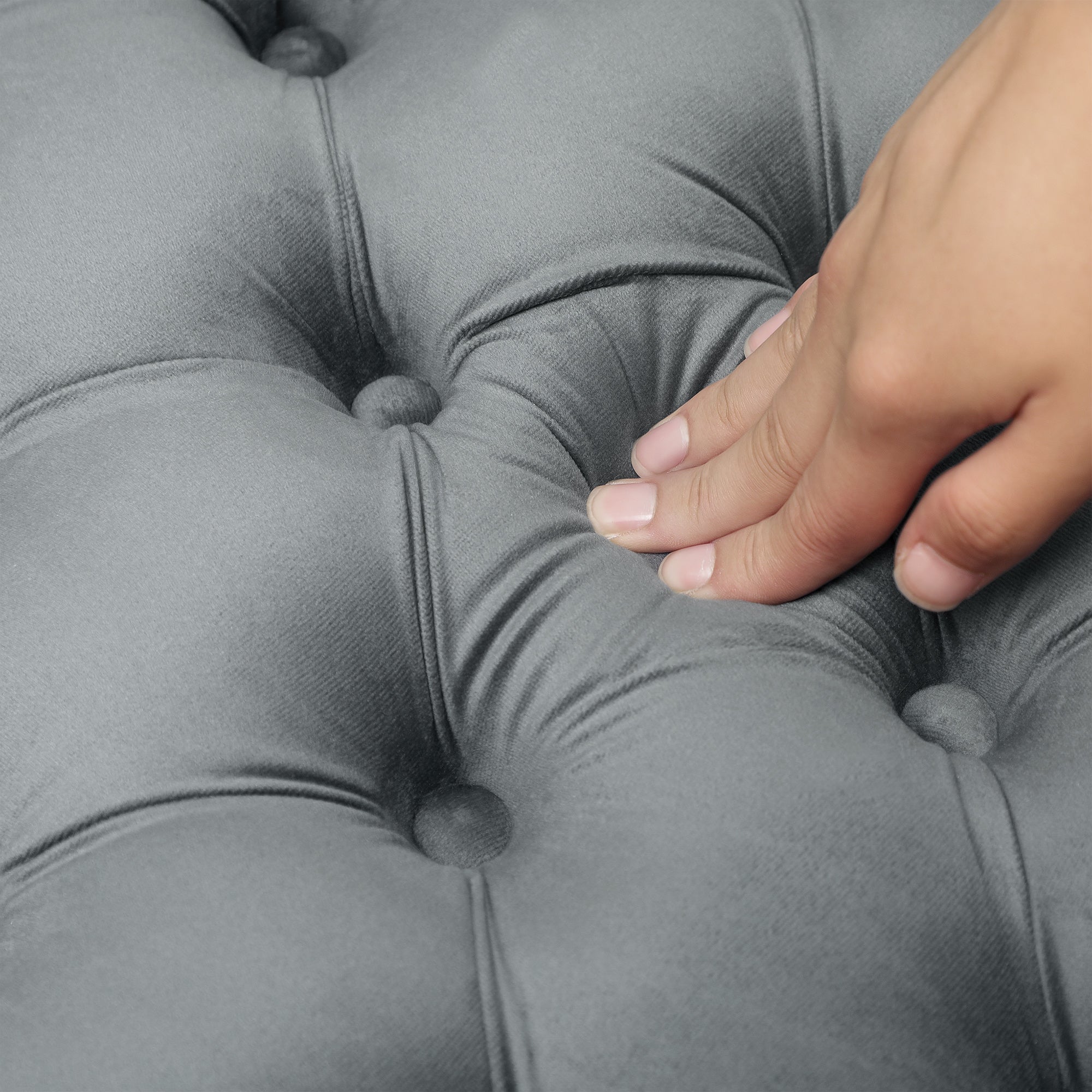 Hand pressing into a gray tufted cushion