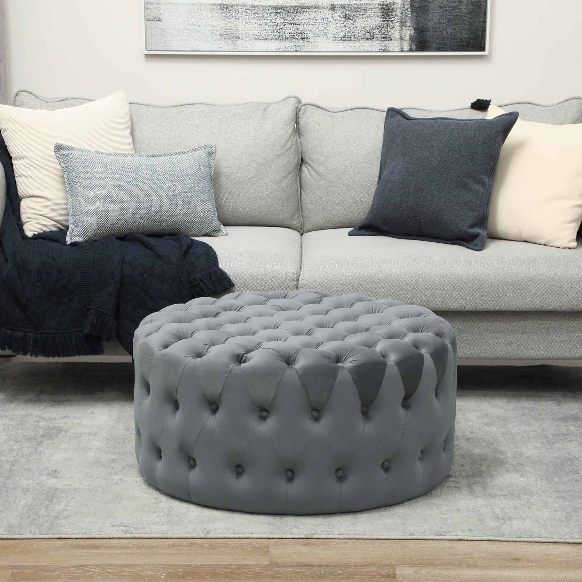 Gray tufted ottoman in front of a gray sofa with cushions in a living room setting.