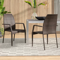 Two wicker chairs in front of a dining table with a wooden wall and rug in the background.